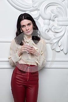 Young woman in red trousers. Beautiful model portrait in front of white studio wall hold wine glass.