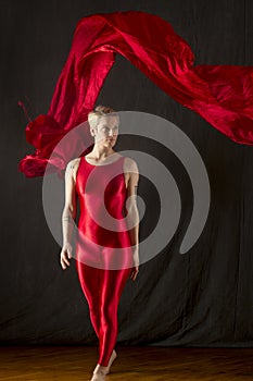 Young woman in red unitard swirling red fabric in studio.