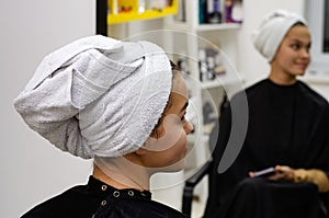 Young woman reflecting in the mirror with a white towel on her head. hair care