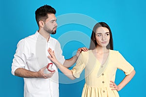 Young woman rejecting engagement ring from boyfriend on background