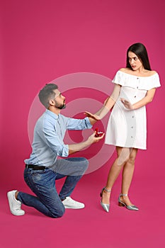 Young woman rejecting engagement ring from boyfriend on crimson background