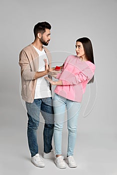 Young woman rejecting engagement ring from boyfriend on grey background