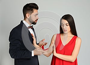 Young woman rejecting engagement ring from boyfriend on light grey background