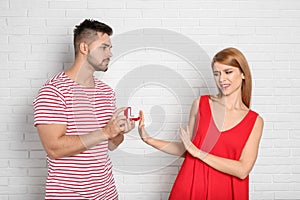 Young woman rejecting engagement ring from boyfriend near brick wall