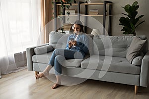 Young woman relax on couch using smartphone