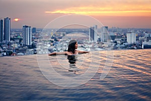 Young woman relax in swimming pool on roof top during amazing sunset and enjoy city view