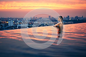 Young woman relax in swimming pool on roof top during amazing sunset and enjoy cityscape