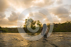 Young woman relaxed at luxury resort infinity pool - happy and cheerful Asian Korean girl in bikini enjoying jungle view at hotel