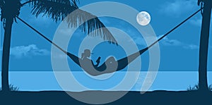 A young woman relaxes in a hammock as she vacations on a tropical beach in the evening moonlight