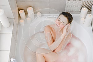 Young woman relaxes in a hot bath full of foam.