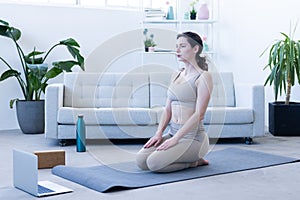 young woman relaxes after yoga exercise on her mat at home in front of her sofa, trainer cools down after showing yoga lessons