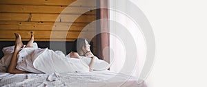 Young woman relaxin in bed near window in cozy log cabin.