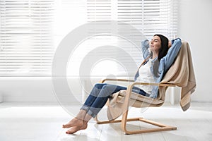 Young woman relaxing in armchair near window