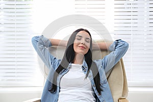 Young woman relaxing in armchair near window