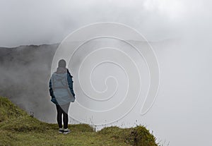 Young woman in relaxing attitude watching a cloudy mountain landscape at the edge of a clif