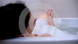 Young woman relaxing in bathroom with foam looking at burning candle.