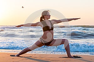 Young woman relaxing on the beach, meditating in warrior asana, at sunset or sunrise and sea Or ocean background, close