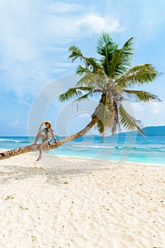 Young woman relaxing at a coconut palm tree on a white tropical beach at La Digue Seychelles Islands