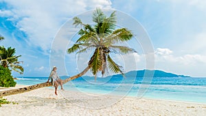 Young woman relaxing at a coconut palm tree on a white tropical beach at La Digue Seychelles Islands