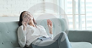 Young woman relaxing on comfortable couch, enjoying listening to lounge music live via smartphone app