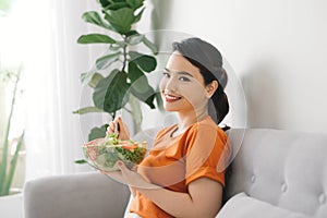 Young woman relaxing on the couch at home and eating a fresh garden salad, healthy lifestyle and nutrition concept