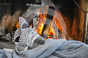 Young woman relaxing in front of cozy fireplace and warming up her feet in woolen socks in country house.