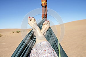 Young woman relaxing in green hammock with view on sand dunes of Sahara Desert, Morocco