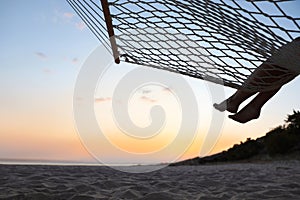 Young woman relaxing in hammock on beach at sunset