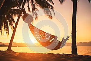 Young woman relaxing in hammock hinged between palm trees on the sand beach at orange sunrise morning time