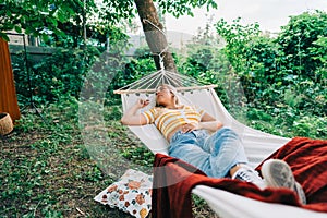 Young woman relaxing in hammock outdoors, in the backyard garden. Enjoying summer