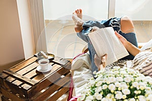 Young woman is relaxing at home, drinking tea, reading book
