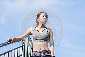 Young woman relaxing after jogging exercise on fence at park.