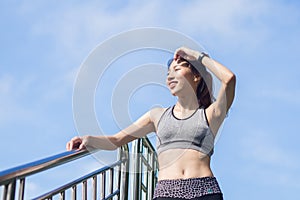 Young woman relaxing after jogging exercise on fence at park to freshen her body and enjoy warm light in morning.