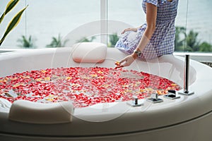 Young woman relaxing on luxury bathtub with roses leaves