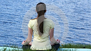 Young woman relaxing meditating on the beach. Girl sitting on the grass and meditate beside the river doing yoga