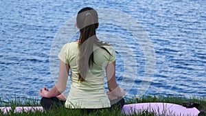 Young woman relaxing meditating on the beach. Girl sitting on the grass and meditate beside the river doing yoga