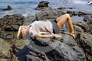 Young woman relaxing and meditating on picturesque rocky seashore