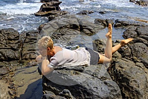 Young woman relaxing and meditating on picturesque rocky seashore