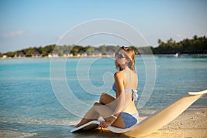 Young woman relaxing in a modern deck chair on a tropical beach with glasses on. Girl is sitting on a beach sun bed