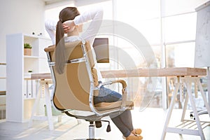 Young woman relaxing in office chair at workplace, back view