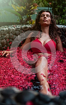 Young woman relaxing in outdoor flower bath, organic skin care, luxury spa in jungle. Beauty and body care. Brunette