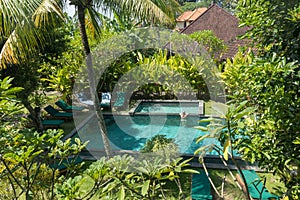 Young woman relaxing in outdoor swimming pool surrounded with lush tropical greenery of Ubud, Bali.