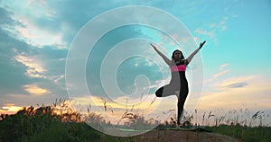 Young woman relaxing outdoors, she do tree position. Woman balansed on one leg at sunset. In harmony of nature.