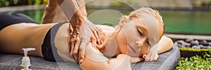 Young woman relaxing outside at a health spa by a swimming pool while having a massage BANNER, LONG FORMAT