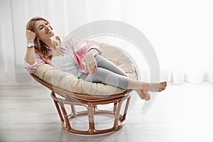 Young woman relaxing in papasan chair near window