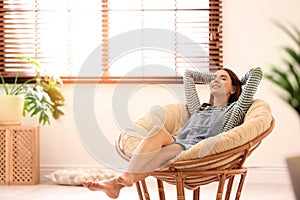 Young woman relaxing in papasan chair near window with blinds at home