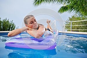 A young woman is relaxing by the pool. in the background a garden and palm trees