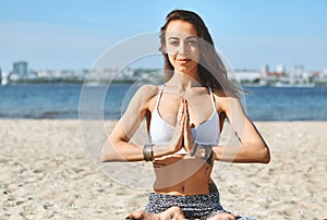 Portrait of a beautiful young woman sitting in lotus pose on the sand city beach with sea background. Feeling so