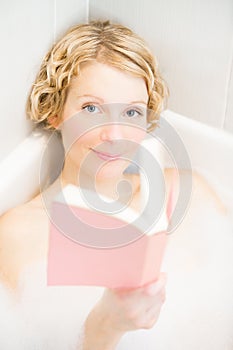 Young woman relaxing and reading a book in the bath