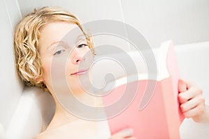 Young woman relaxing and reading a book in the bath